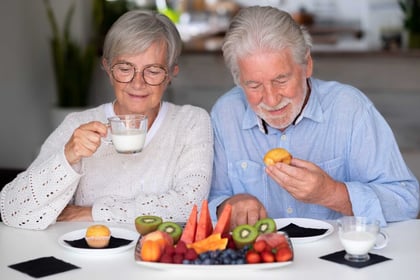 Senior couple having breakfast at home with fresh seasonal fruit, milk and cupcake
