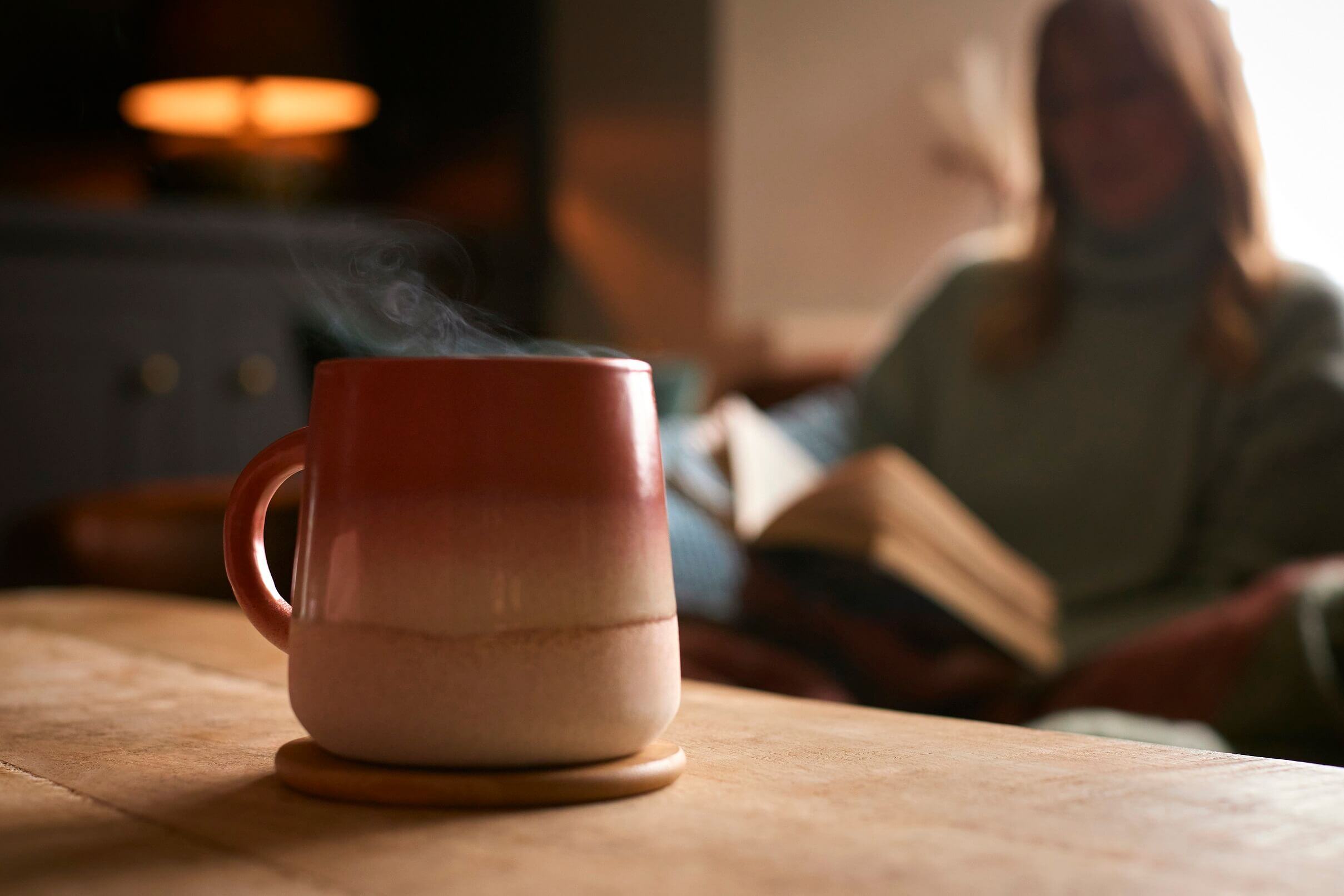 a person sat reading a book with a hot drink